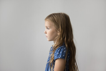 Side profile view serious little girl standing against gray studio background, staring straight, looks concerned or focused, thinking, deep in thoughts. Childhood, kids issues or education services ad