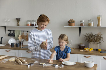 Young redhead woman and preschooler 6s daughter make dough for sweet dessert on weekend at home,...