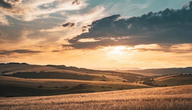 sky with beautiful clouds over rolling hills with stubble field at sunset in summer