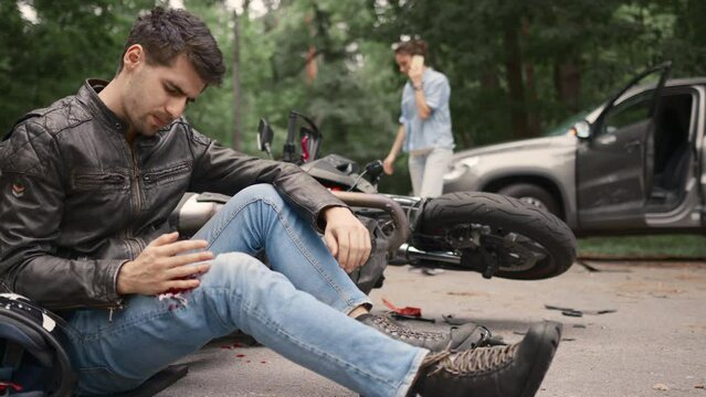 Motorcyclist sits on the asphalt near motorcycle, after road accidents with car. Broken and wrecked motorcycle on road