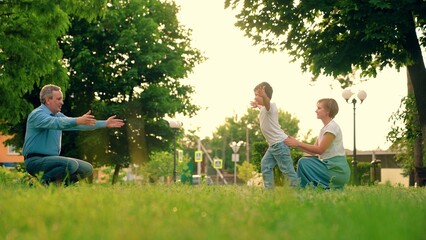 Parents childhood, joyful hugs of child to mother. Family, kid boy playing on lawn. Child, son runs from mom to dad , hugs her in park. Happy family, Kid. Child plays outdoor in spring with his dad