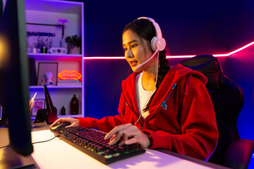 Host channel of beautiful Asian girl streamer concentrating online game wearing headphones pastel color talking with viewers media online. Esport skilled team players in neon blue room. Stratagem.
