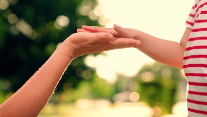 Child hand greets mom hand in park. Mom plays with his little child, teaches his daughter how to say hello, hello mom. Mother, boy child together. Happy family. Boy kid dad shakes hands in park, walk