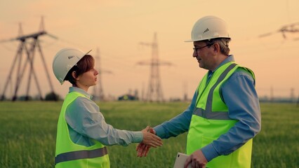 Handshake on background of power line. Civil engineers, electrical engineers sign contract digital tablet against background of high-voltage electrical line. Successful business, teamwork, cooperation