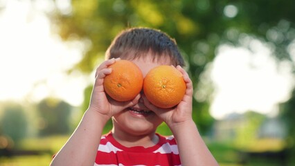 Portrait cheerful little kid hold juicy oranges in hands. Small baby close-up play ripe oranges. Healthy food for kids. Healthy fruits from garden summer. Happy healthy kids. Concept healthy nutrition