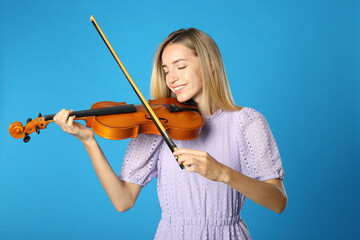 Beautiful woman playing violin on blue background