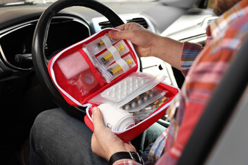 Man holding first aid kit with medicaments inside car, closeup