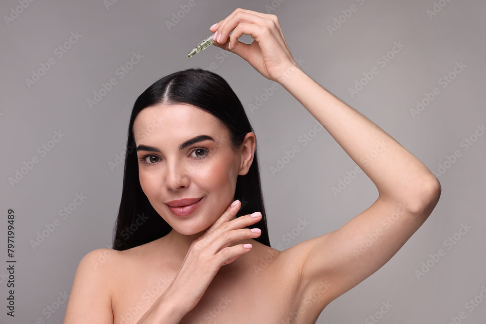 Sticker Beautiful young woman using ampoule for hair treatment on grey background