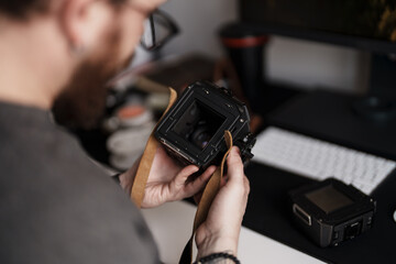 Close-up of a professional photographer carefully inspecting the details of a medium format camera against a modern office backdrop.