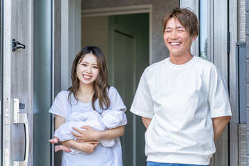 玄関で出迎える赤ちゃんを抱っこする若いアジア人夫婦
