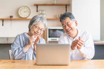 パソコンを使ってビデオ通話・テレビ電話する笑顔のシニア・高齢者夫婦
