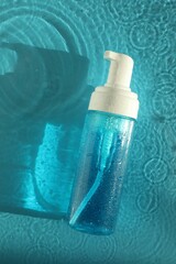 Bottle of cosmetic product in water on turquoise background, top view