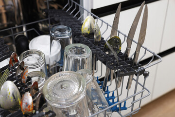 Open modern dishwasher with dirty tableware in kitchen, closeup