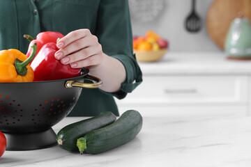 Woman taking bell pepper from black colander at white marble table in kitchen, closeup. Space for...