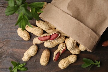 Paper bag with fresh peanuts and leaves on wooden table, flat lay
