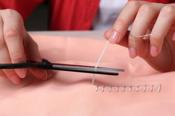 Woman cutting sewing thread over cloth, closeup