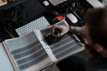 A tattooed photographer carefully examines film negatives at a well-organized desk with photography equipment.