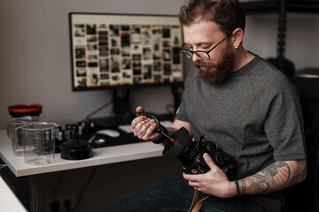 Focused male photographer carefully cleaning the lens of a professional camera at his organized, contemporary workspace.