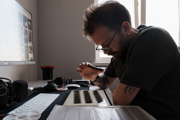 A focused photographer examines film negatives with a magnifying glass on a lighted worktable, surrounded by photography equipment.