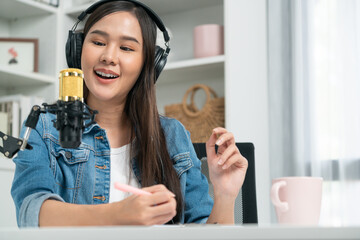 Host channel Asian influencer talking in broadcast streaming online wearing headset on social media live with script note, greeting listeners in life coaching or marketing at modern studio. Stratagem.