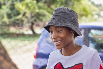 village african teenager girl with a a hat, standing in the yard , car in the background