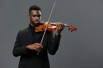 African American man in black suit playing violin on gray background in elegant musical performance
