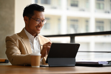 Smiling male entrepreneur in eyeglasses using digital tablet on an office building patio