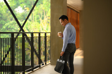 Smiling young businessman with briefcase walking through a corridor of an office building - 797236069