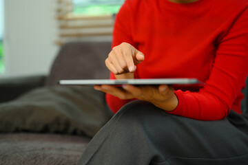 Cropped shot young woman in red sweater using digital tablet on couch at home - 797237819