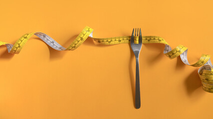 Fork with measuring tape on yellow background. Weight loss and healthy lifestyle concept - 797238428