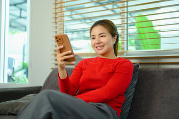 Pleased young woman using mobile phone on couch at home - 797239021