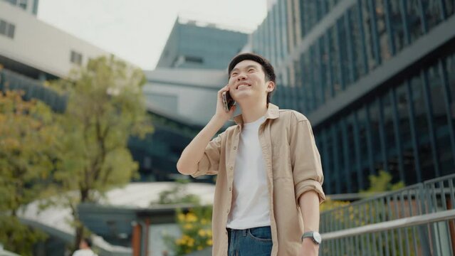 Handsome Asian student using smartphone. A young man standing outdoor happy smiling with holding mobile phone