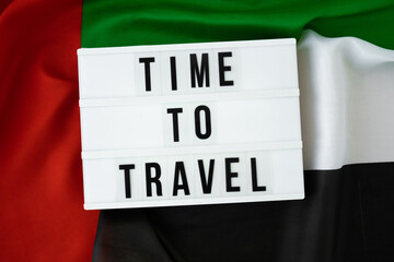 Message with text TIME TO TRAVEL on background of waving UAE flag made from silk. United Arab Emirates flag with concept of tourism and traveling. Inviting greeting card, advertisement. Dubai