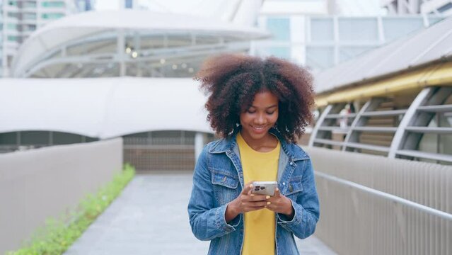 Black young woman using smart phone and smile with walking in the city outdoor. Happy african student, young female walking with mobile by a building