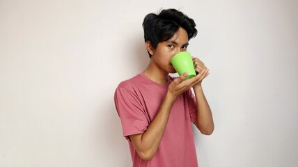 young asian man posing drinking from a cup on an isolated white background. drink water or coffee...