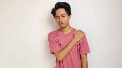 Young Asian man holds his shoulder as if he is in pain with an isolated white background