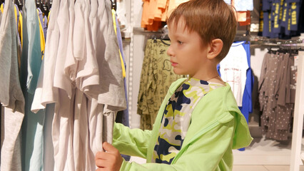 A cute boy chooses a t-shirt in a clothing store