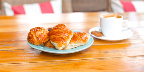 Croissant banner on a blue plate on a wooden table next to coffee. Delicious fresh pastries and desserts for breakfast.