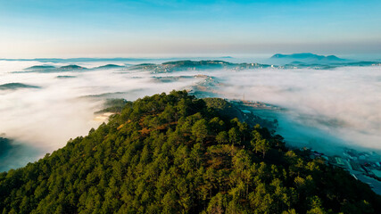 A lush green forest covers a mountain in the morning. The forest is shrouded in mist.