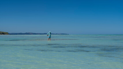 The man is standing knee-deep in water. The endless aquamarine ocean stretches to the horizon. Islands in the distance. Clear blue sky. Copy space. Madagascar. Nosy Iranja