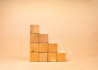 Arrows jumping down on wood cube graph step blocks, decrease business graph step on beige background. Financial crisis, bankruptcy, loss investment economic recession sales risk concepts.