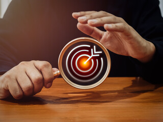 Target, red bullseye dartboard icon inside magnifying glass in businessman hand for focus business goals and trends on wood table. Business marketing strategy, leadership concept, minimal style.