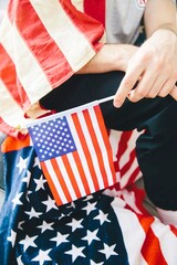 The image shows a person holding a small American flag. The flag is red, white, and blue, with the...