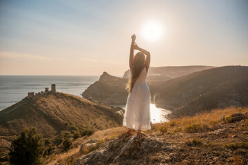 woman stands on a hill overlooking the ocean, her arms raised in the air. Concept of freedom and joy, as if the woman is celebrating a moment of happiness or accomplishment.