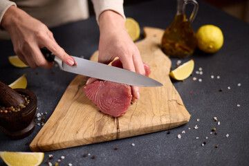 Woman cut tuna steak into slices on a wooden cutting board at domestic kitchen cooking tuna...