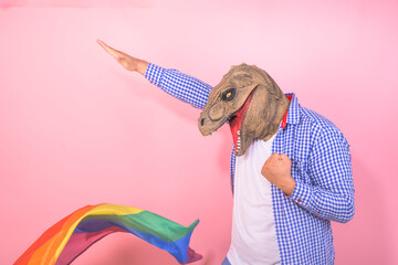 man in dinosaur mask with funny pose with a rainbow flag on isolated pink background