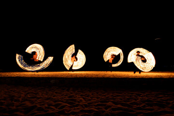 Silhouetted performers with flaming poi creating a stunning visual effect on the shore by four dancers in row
