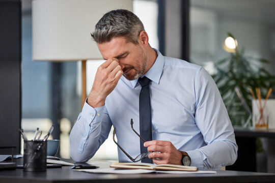 Anxiety, headache or stress with business man at desk in office for audit, compliance or tax. Burnout, depression and mental health with mature employee in pain at corporate or professional workplace