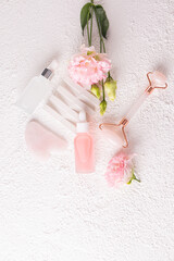 Set of cosmetics for massage and skin care of face and neck on white background with pink flowers. Two bottles of serum and oil. Massager. gua sha.