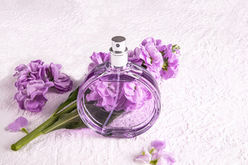 A chic bottle of women's perfume and a delicate lilac color flower. Front view. Unnamed bottle for...